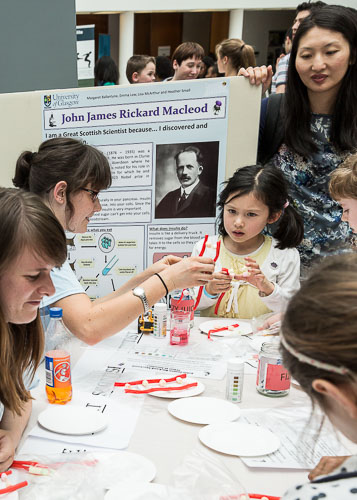 Photograph showing 2 GSF in Action students creating DNA out of sweets with a child and parent. 