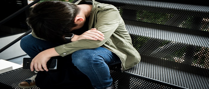 A teen sitting in despair, with a cell phone, head in his hands