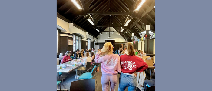 Two females with their backs to the camera in a room of students 