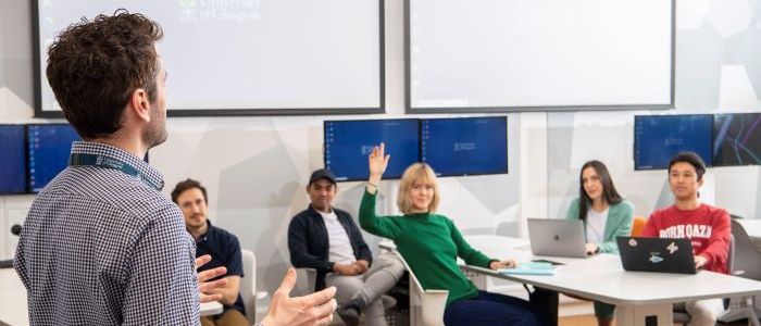 Lecturer in discussion with students at desk asking questions