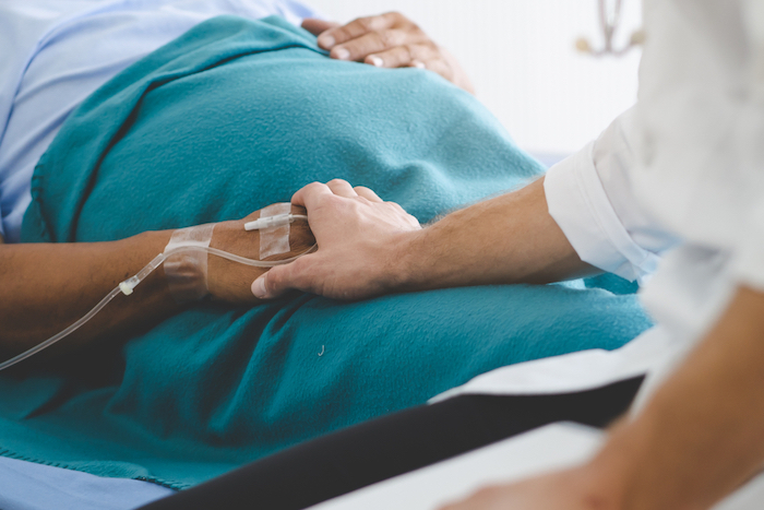 A person touching the hands of a patient in a hospital bed
