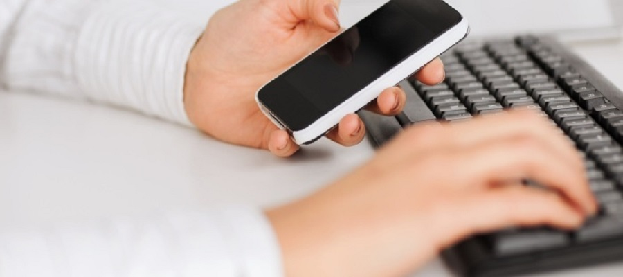 Hands holding a phone and typing on keyboard