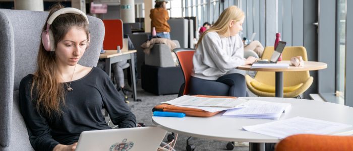 Two female students studying on comfy chairs at a table in the James McCune Smith building