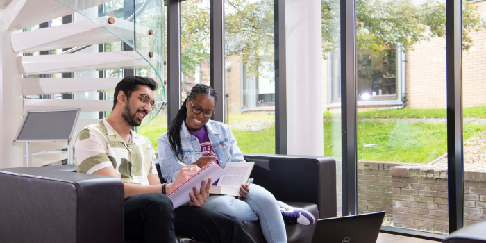Two students sitting on a sofa laughing and studying in the library