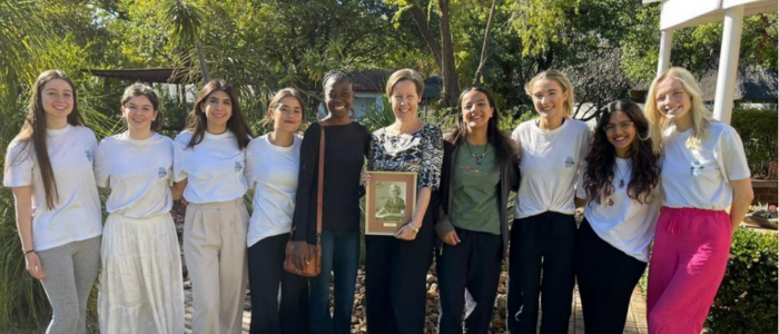 A group of students from UofG FemEng smiling in a line. In the centre are Eunice Ntobedzi Hannah and High Commissioner Sian Price. Sian Price holds a frame in which sits a portrait of Eleanor Emery.