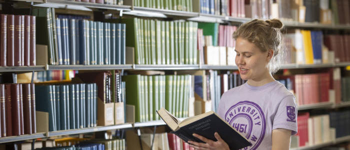 Student consulting a book from the library shelf